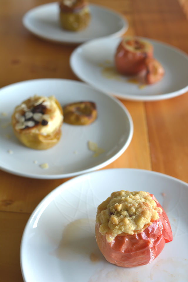 an image of four freshly baked apples, one of them showcasing the berry crumble topping