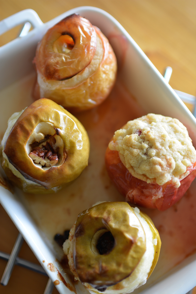 verhead view of four freshly baked apples, with two red apples and two green apples, each topped with a different delicious topping