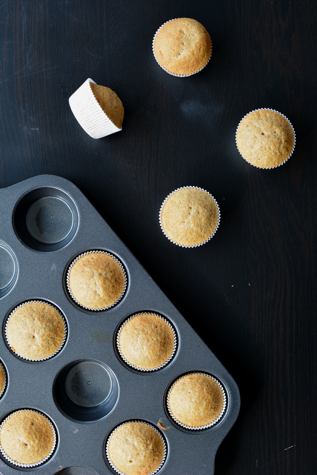 top-down view of a cupcake baking tray filled with freshly baked cupcakes, with some cupcakes placed beside the tray