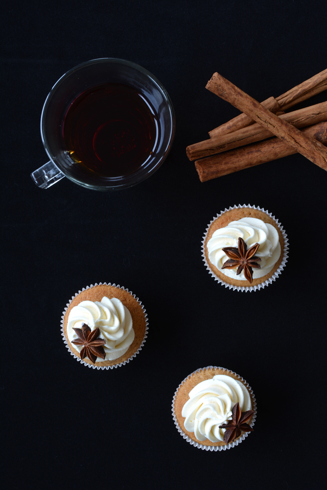 top view image of three chai tea spiced cupcakes adorned with luscious buttercream frosting and garnished with star anise, accompanied by a cup of steaming tea placed beside them.