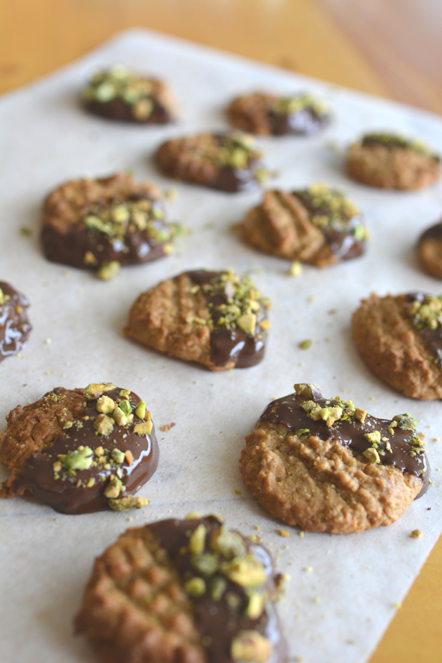 group of peanut butter, chocolate and pistachio cookies with a half-dipped chocolate coating and garnished with crushed pistachios