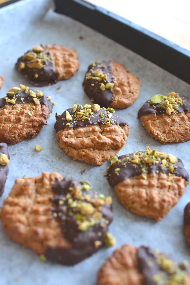 group of peanut butter, chocolate and pistachio cookies with a half-dipped chocolate coating and garnished with crushed pistachios