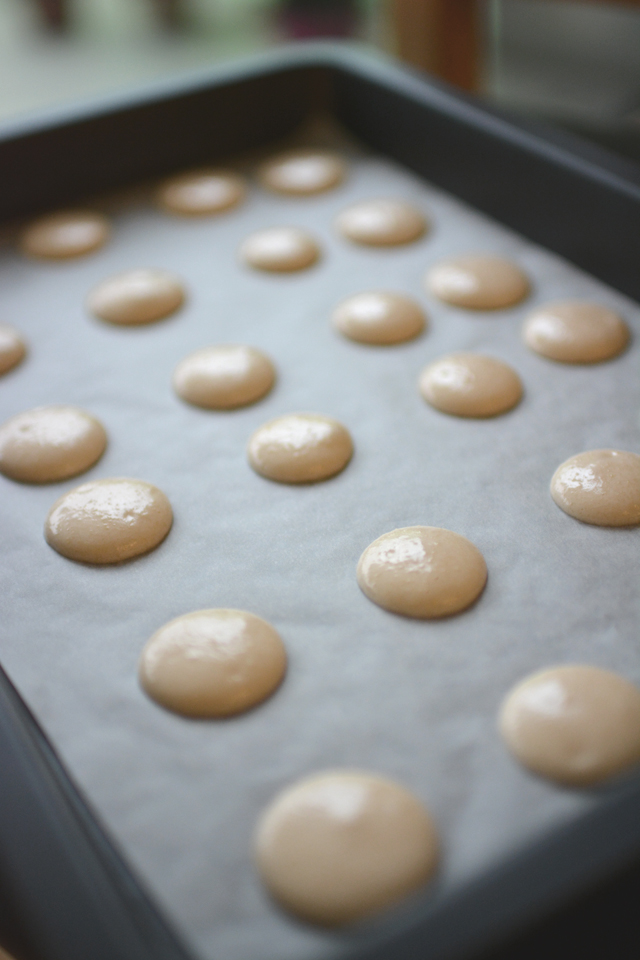 close-up of a baking tray filled with macaron mixture, arranged on a template for the drying process