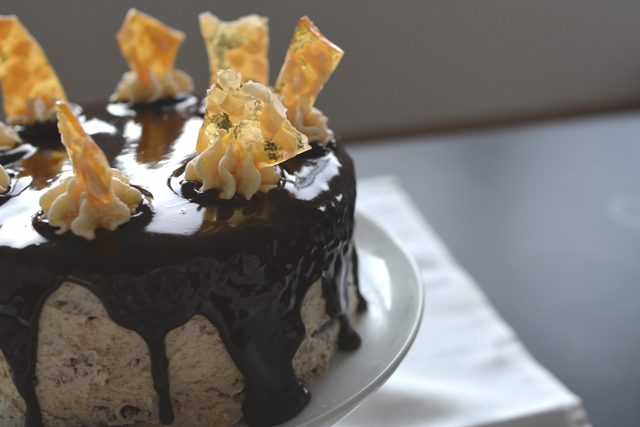 half-view image of a finished chocolate praline cake, drizzled with ganache and topped with buttercream and praline