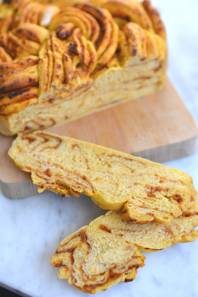 close-up image of a freshly baked sweet potato and sun-dried tomato braided bread resting on a cutting board, with two slices cut from it
