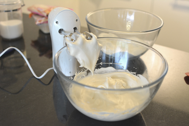 image of a bowl containing stiff peak mixture, with a hand mixer resting nearby