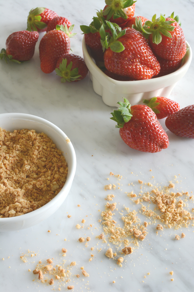 an image of a bowl filled with fresh strawberries, some of which are scattered on the table next to another bowl containing crushed nuts