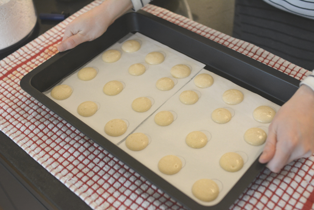 hands gently tapping a baking tray filled with macaron mixture before baking
