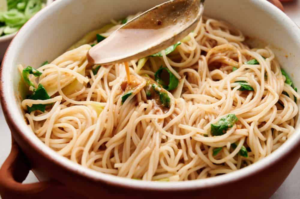 A spoon pouring peanut sauce over Cold Asian Noodle Salad in a bowl.