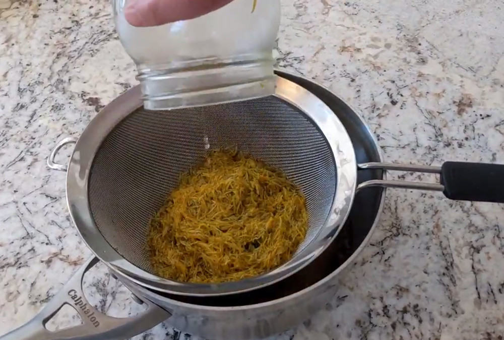 Dandelion tea being pour from a jar into a strainer that's being held by a pot.