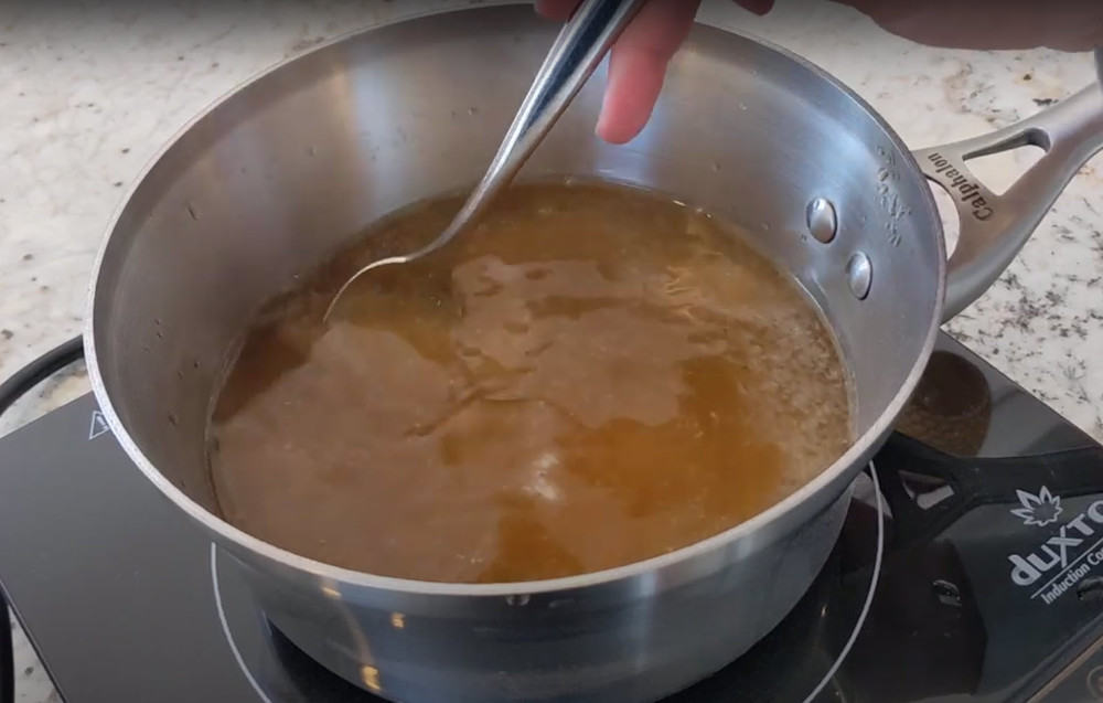 Dandelion tea in a bot on an electric burner boiling and being stirred by a woman's hand.