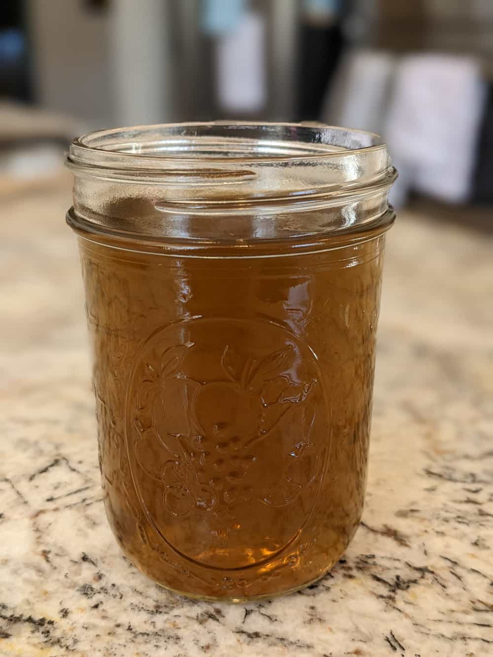 Finished dandelion jelly poured into a jar and sitting on a granite countertop.