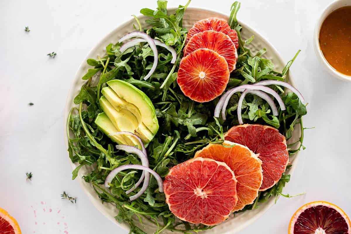 Assembling a winter citrus salad on a white plate, top view.