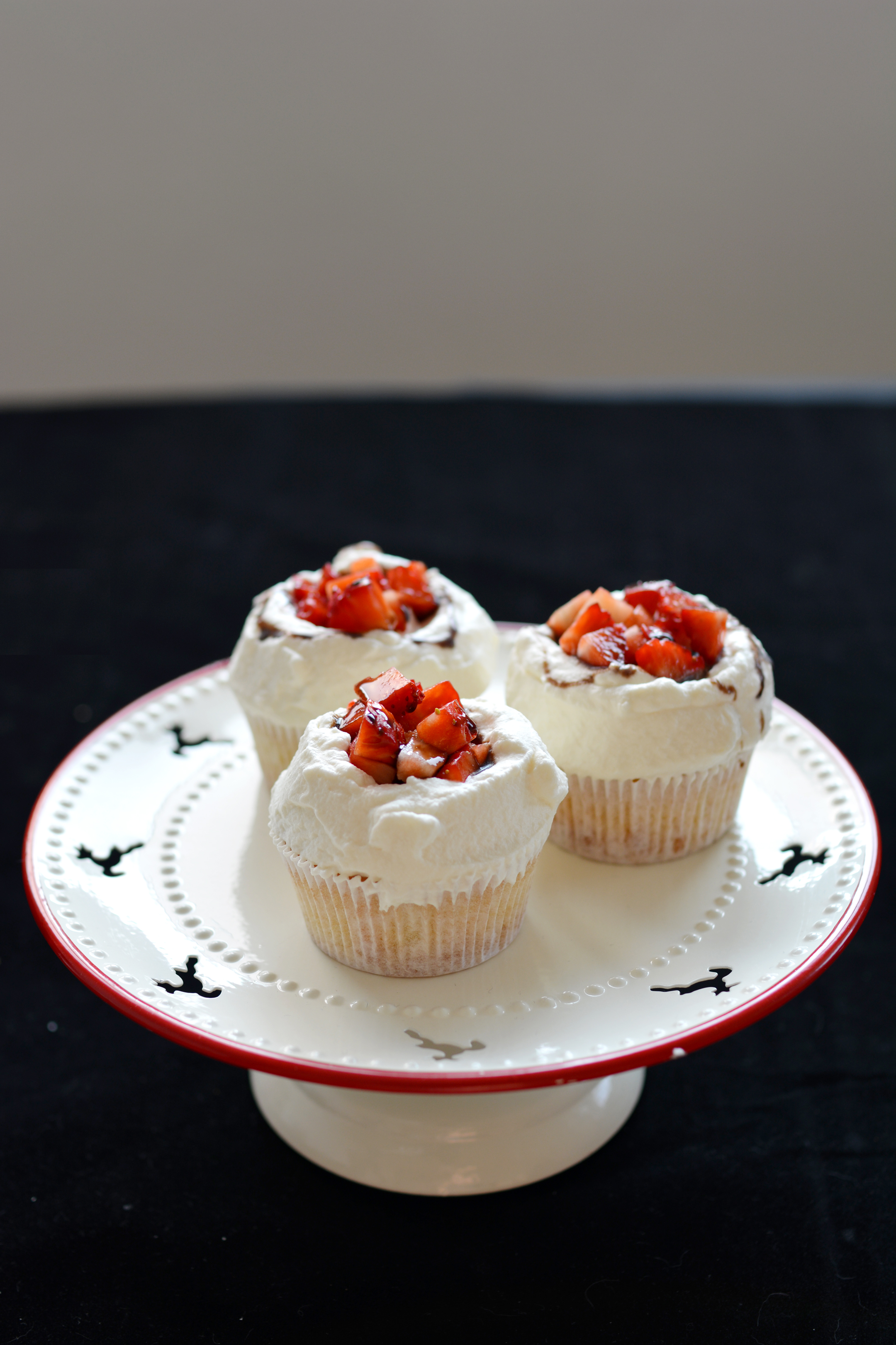 close-up view image of three cupcakes with fresh cream, strawberries, and balsamic vinegar glaze, beautifully presented on a cake table