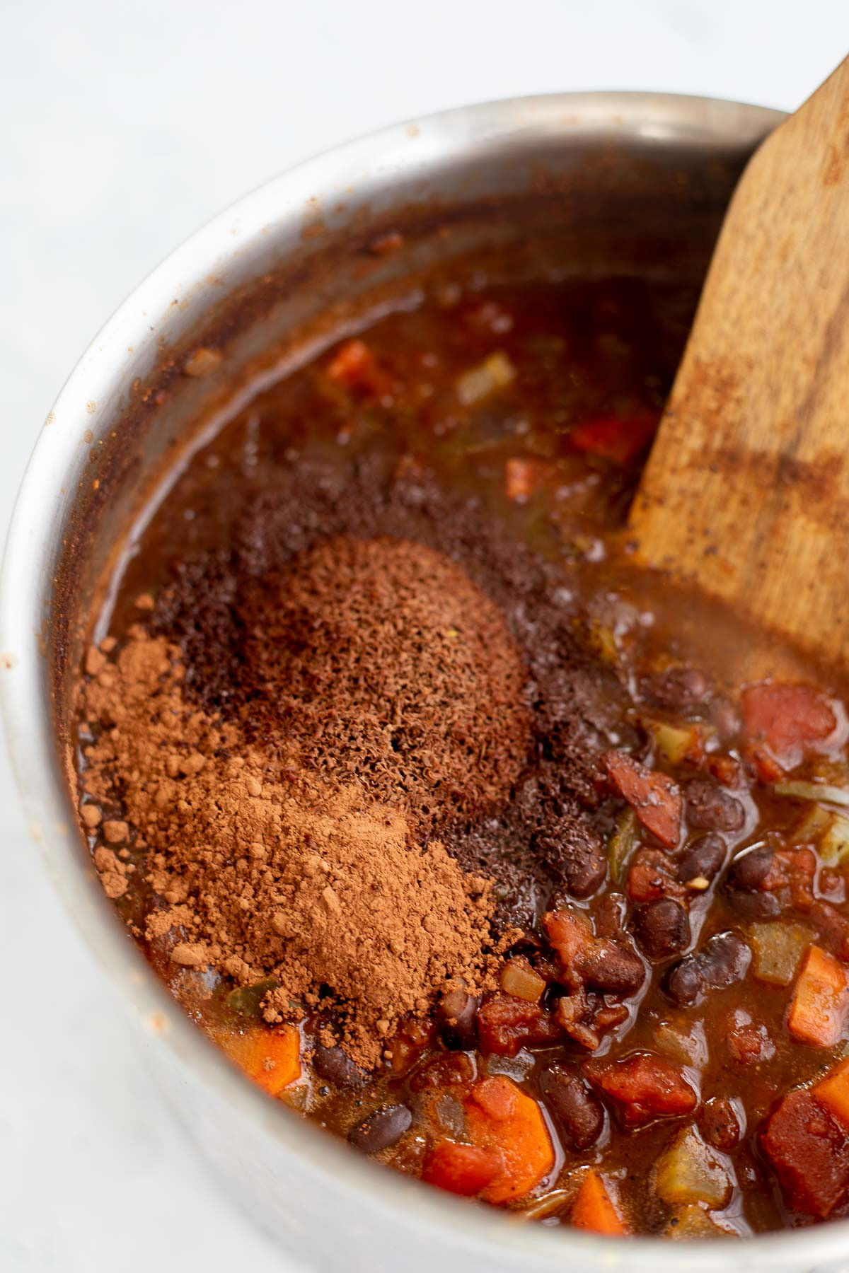 Ingredients for Black Bean Chili with Chocolate being stirred in a pot with a wooden spoon.