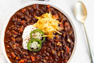 Black Bean Chili with Chocolate in a white bowl garnished with jalapeno slices, sour cream, and shredded cheddar, top view.