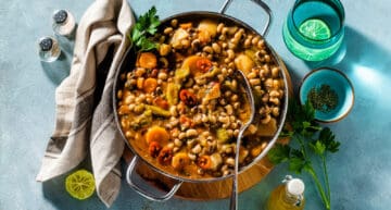 Black-eyed Pea soup in a metal pan on a wooden stand on a blue background.