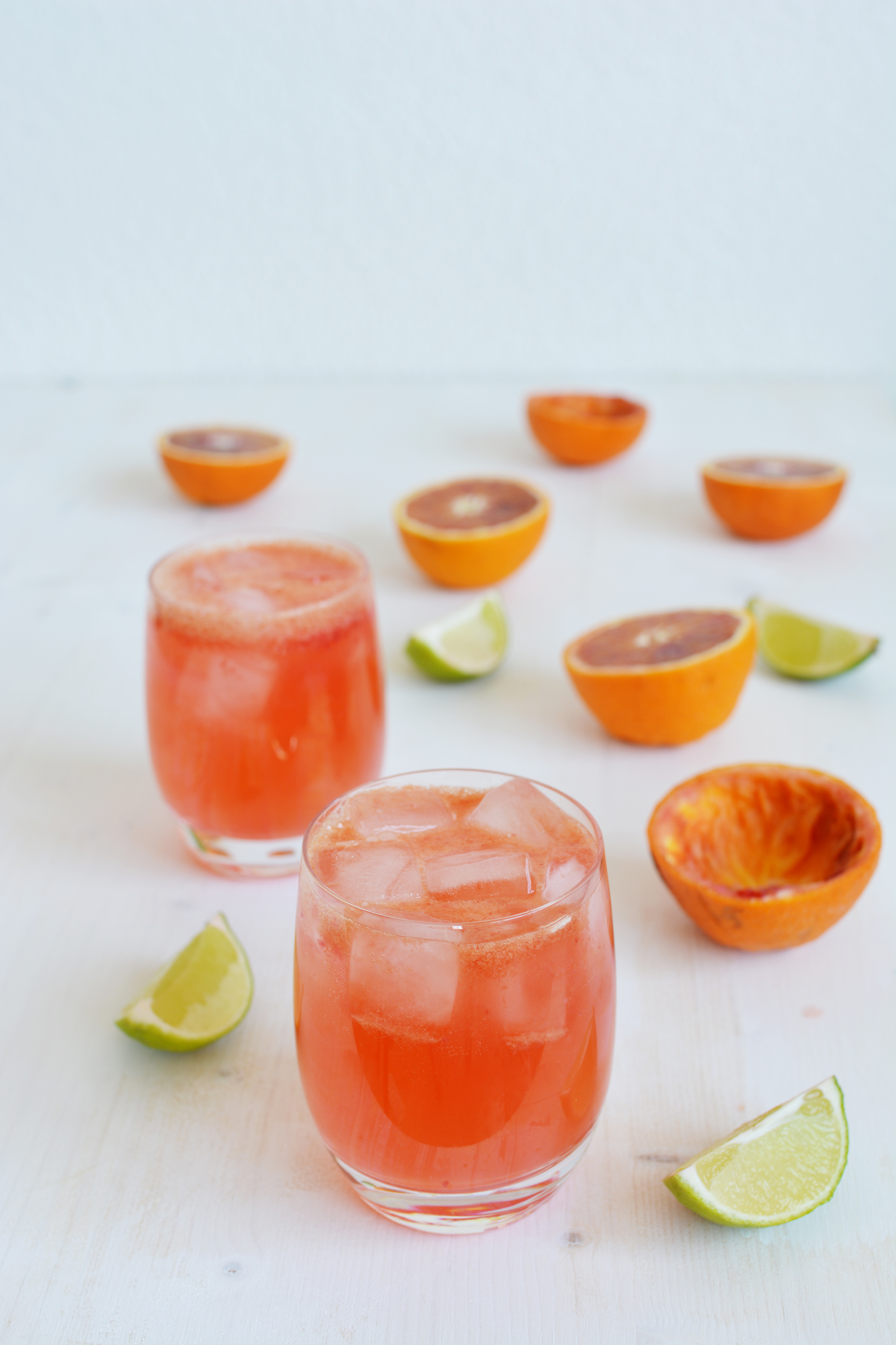 an image of two glasses of blood orange gin and tonic, garnished with lime and blood orange slices
