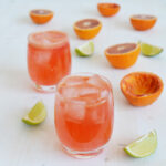 a cropped image of two glasses of blood orange gin and tonic, garnished with lime and blood orange slices