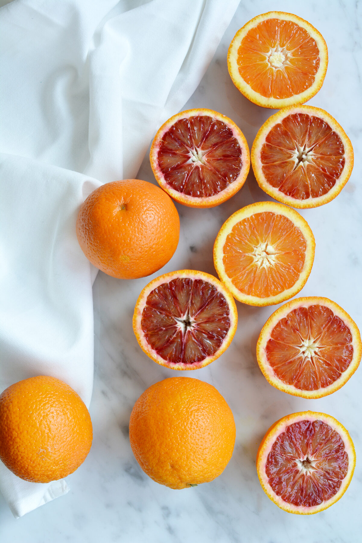 Several blood orange, some whole and some cut in half, displayed on a marble countertop. 