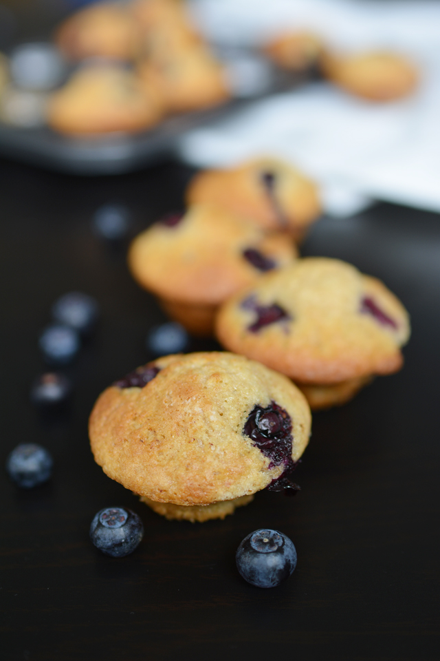 a detailed shot of brown butter and blueberry mini muffins, highlighting the luscious blueberry toppings with fresh blueberries nearby