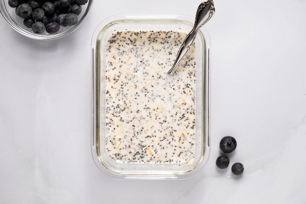 Blueberry overnight oats mixture being stirred with a spoon in a glass container before placing in the refrigerator.