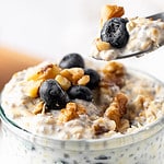 Closeup view of a spoonful of Blueberry Overnight Oats begin taken from a glass jar.