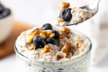 Closeup view of a spoonful of Blueberry Overnight Oats begin taken from a glass jar.