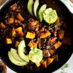 Black Bean and Butternut Squash Chili in a Dutch oven topped with Avocado and lime.