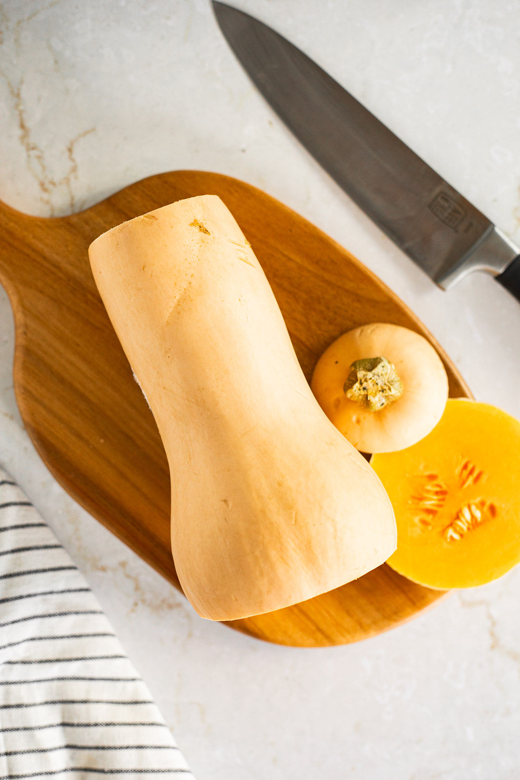 A butternut squash on a cutting board with the top and bottom cut off.