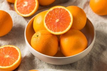 Several Cara cara navel oranges, some whole and some cut in half, and some in a bowl and some on a table with a white tablecloth.