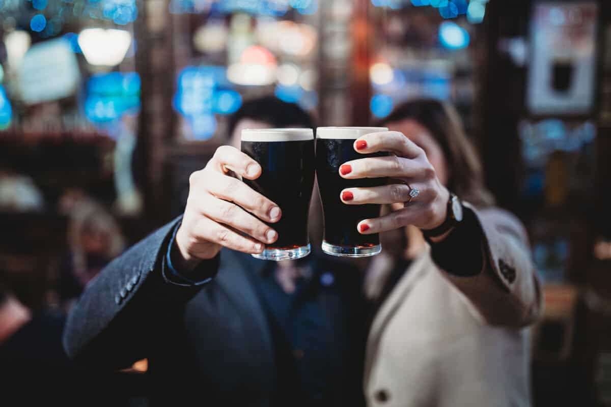 A couple holding glasses of beer and cheering.