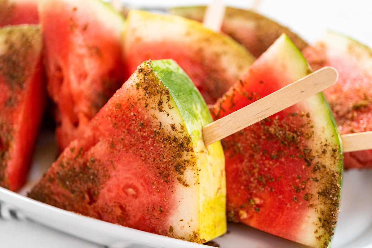 Pieces of watermelon on popsicle sticks seasoned with Tajin chili lime seasoning.