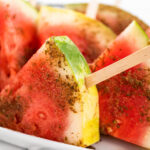 Pieces of watermelon on popsicle sticks seasoned with Tajin chili lime seasoning.