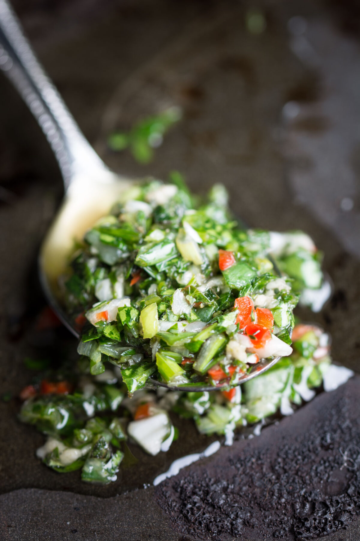 Close-up view of fresh Chimichurri sauce on a spoon with a black background.