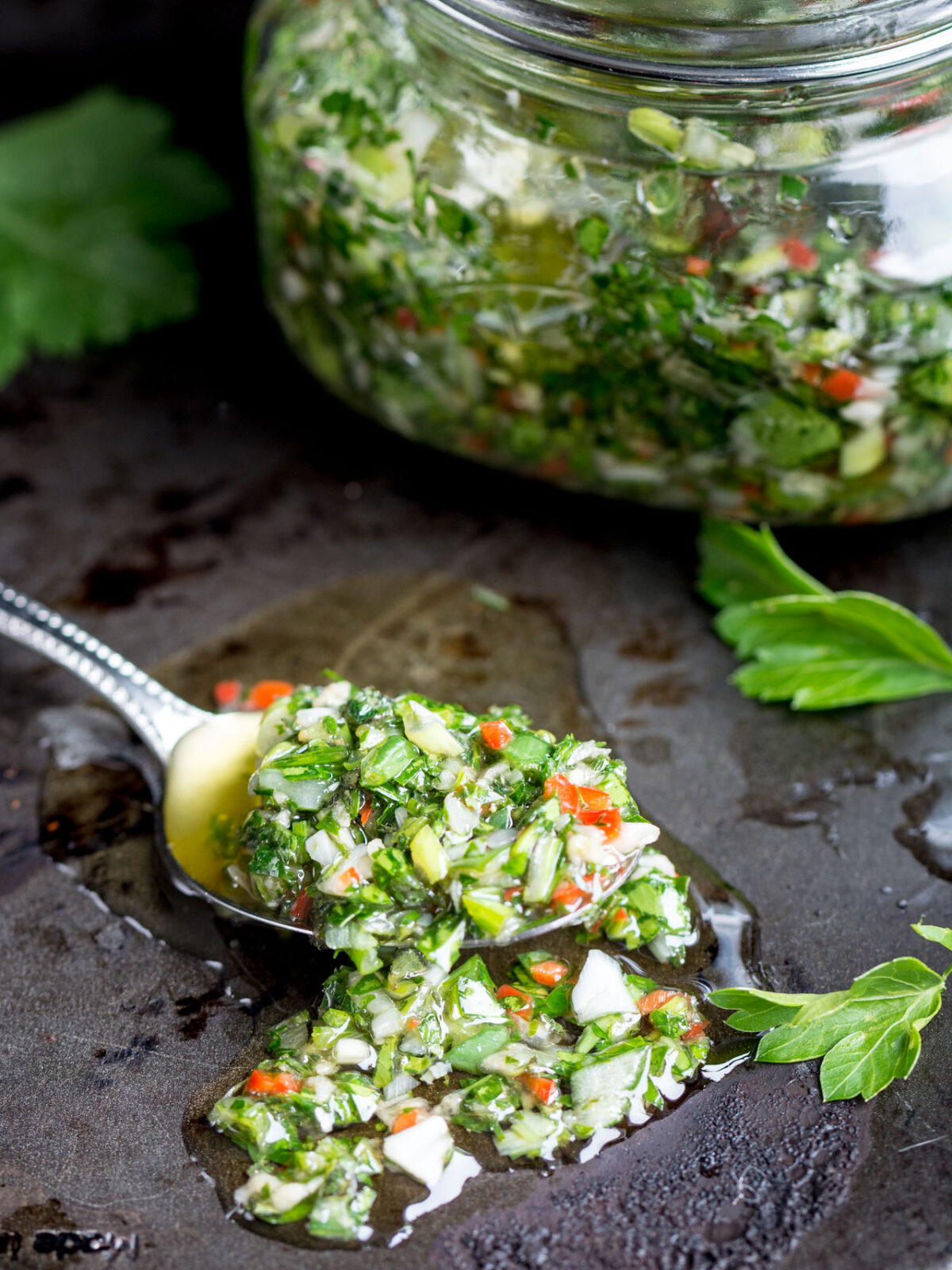 Fresh Chimichurri sauce on a spoon with a black background.