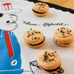 flatlay view of four chocolate coffee macarons arranged on a tea towel, each topped with decadent chocolate chunks