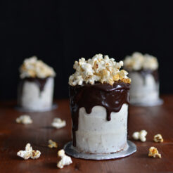 close-up image of a chocolate cake with chocolate syrup drizzle, topped with chili popcorn, and two additional cakes arranged on top of a champagne glass