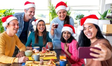 A group of people wearing Santa hats are sitting and standing around a table with breakfast food.