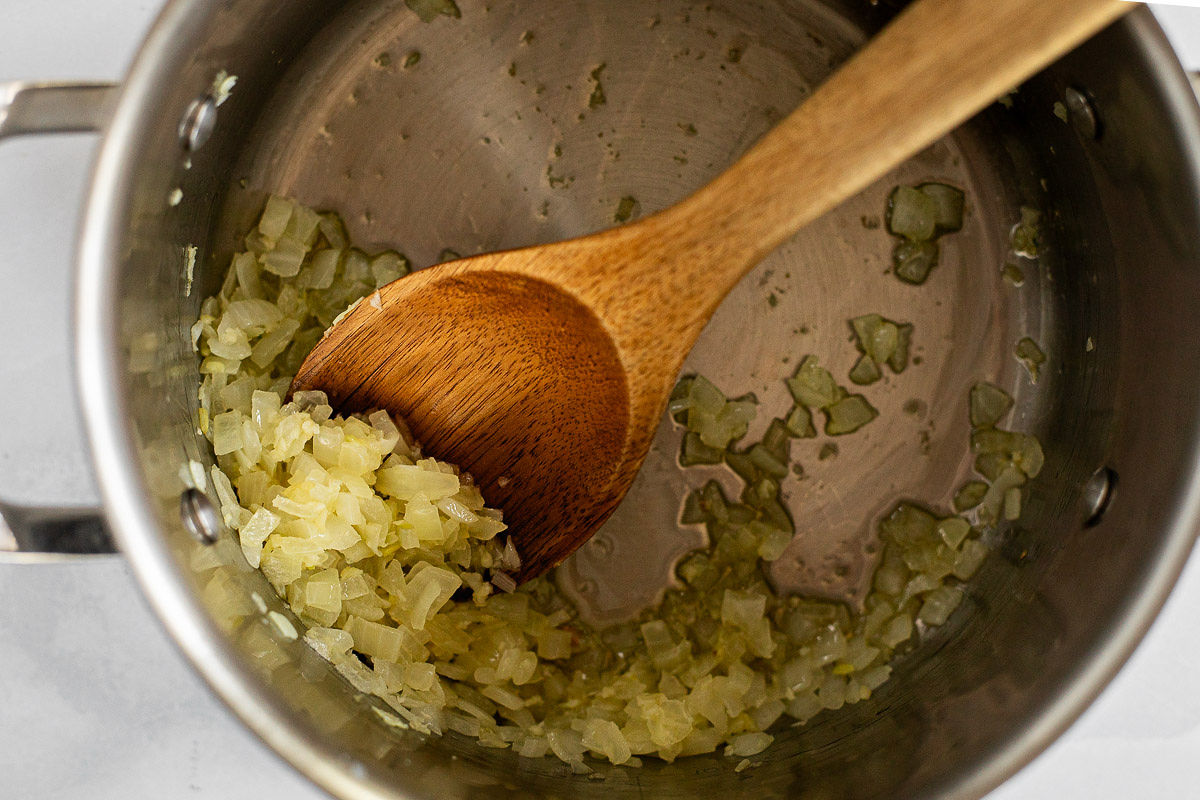 A soup pot with sautéed onions and a wooden spoon.