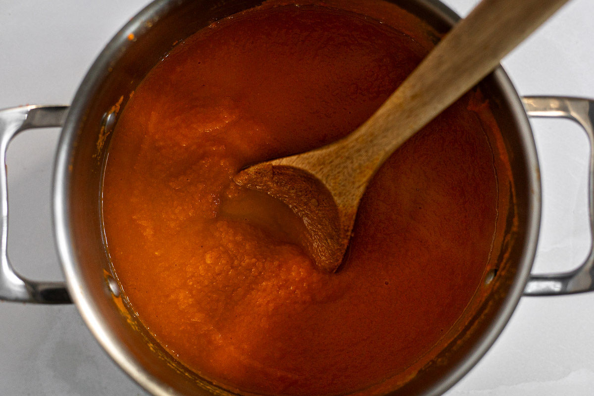 The blended soup in a soup pot with a wooden spoon.