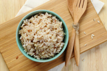 Cooked brown rice in a bowl on a cutting board with wooden utensils.