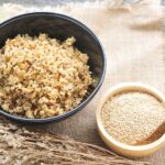 Bowl of cooked quinoa with a smaller bowl of raw quinoa and a dried plant.