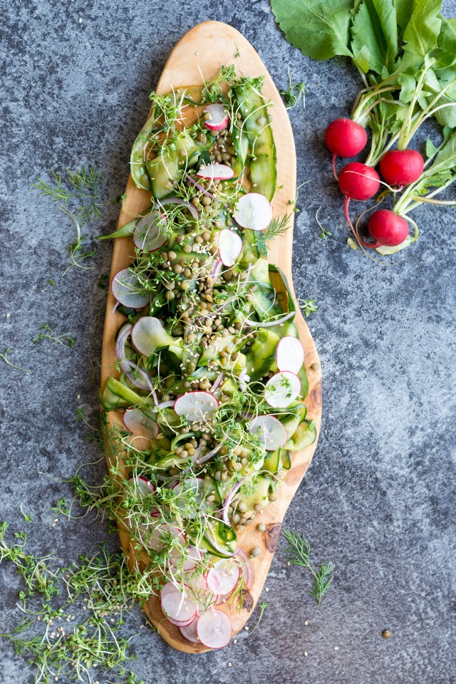 Top view of a cucumber and lentil salad with radishes on a wooden board and a bunch of radishes on the side. 