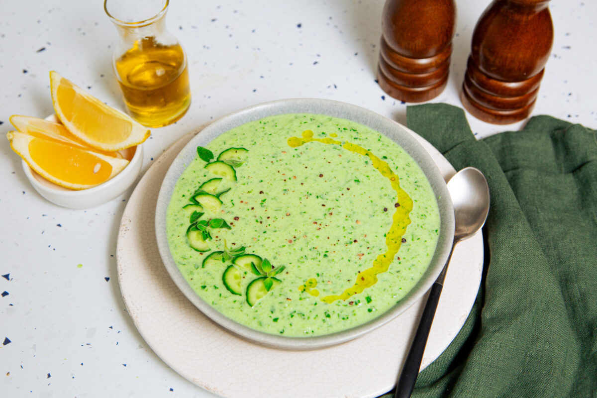 Cold cucumber soup in a white bowl garnished with sliced cucumbers and olive oil.