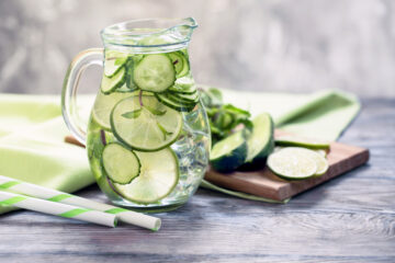 A glass pitcher filled with cucumber water, flavored with lime and mint.