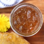 An overhead view into a jar of dandelion jelly with a dandelion flower blurred in the background.