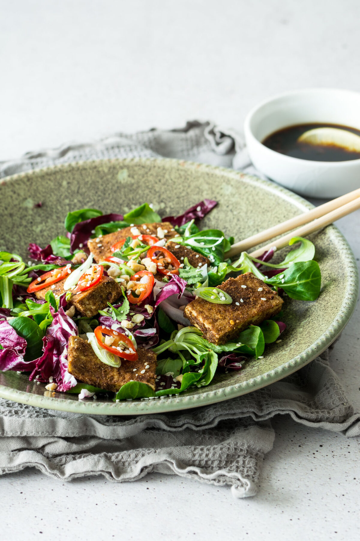 close up image of a dry-rubbed tofu salad, mixed greens, tomatoes, cucumbers, and carrots. drizzled with vinaigrette, crushed peanuts
