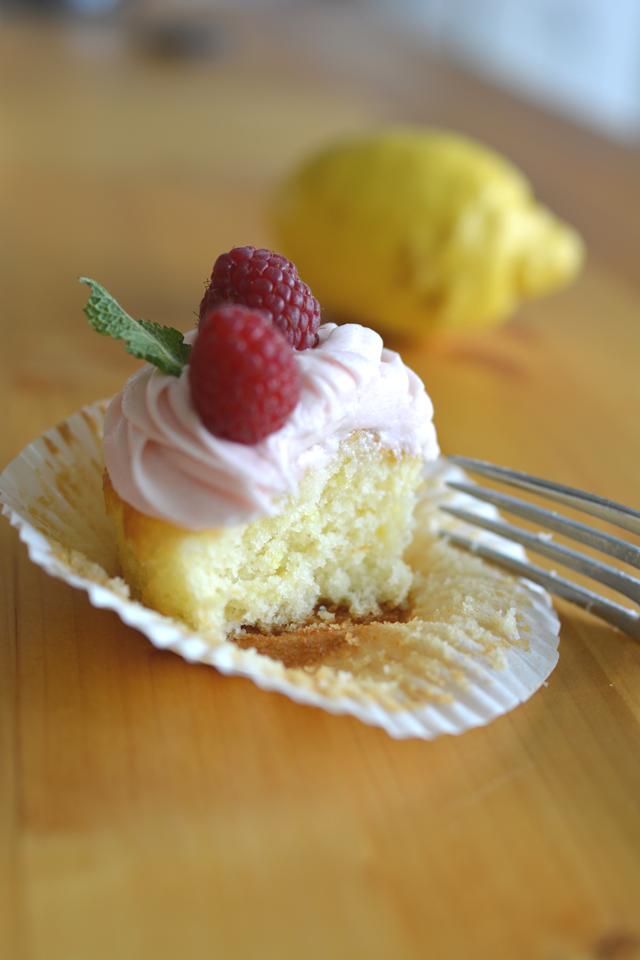 an image of one sliced lemon and raspberry cupcake topped with icing and fresh rapsberries 