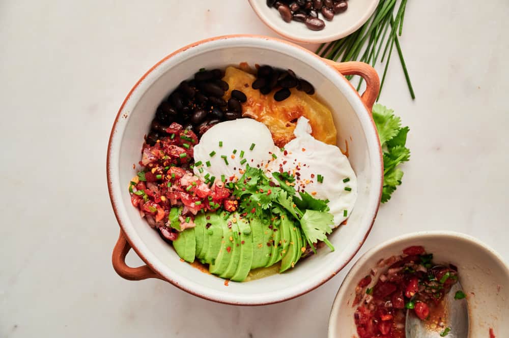 Healthy Spanish Huevos Rancheros with poached eggs, avocadoes, black beans, salsa, and cheesy potatoes.